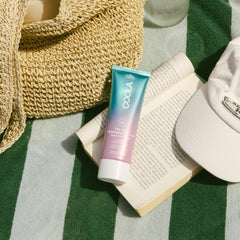 COOLA bottle on beach towel conveying outdoor use and sun-ready protection