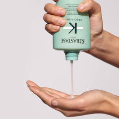 KÉRASTASE bottle held next to hand showing true size for accurate purchase decision benefit