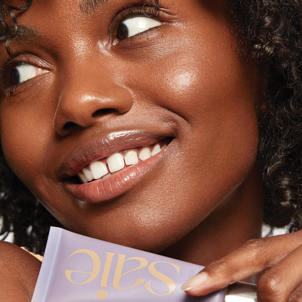 Saie Sunvisor swatch on hand showing sheer golden pearl and glow benefit