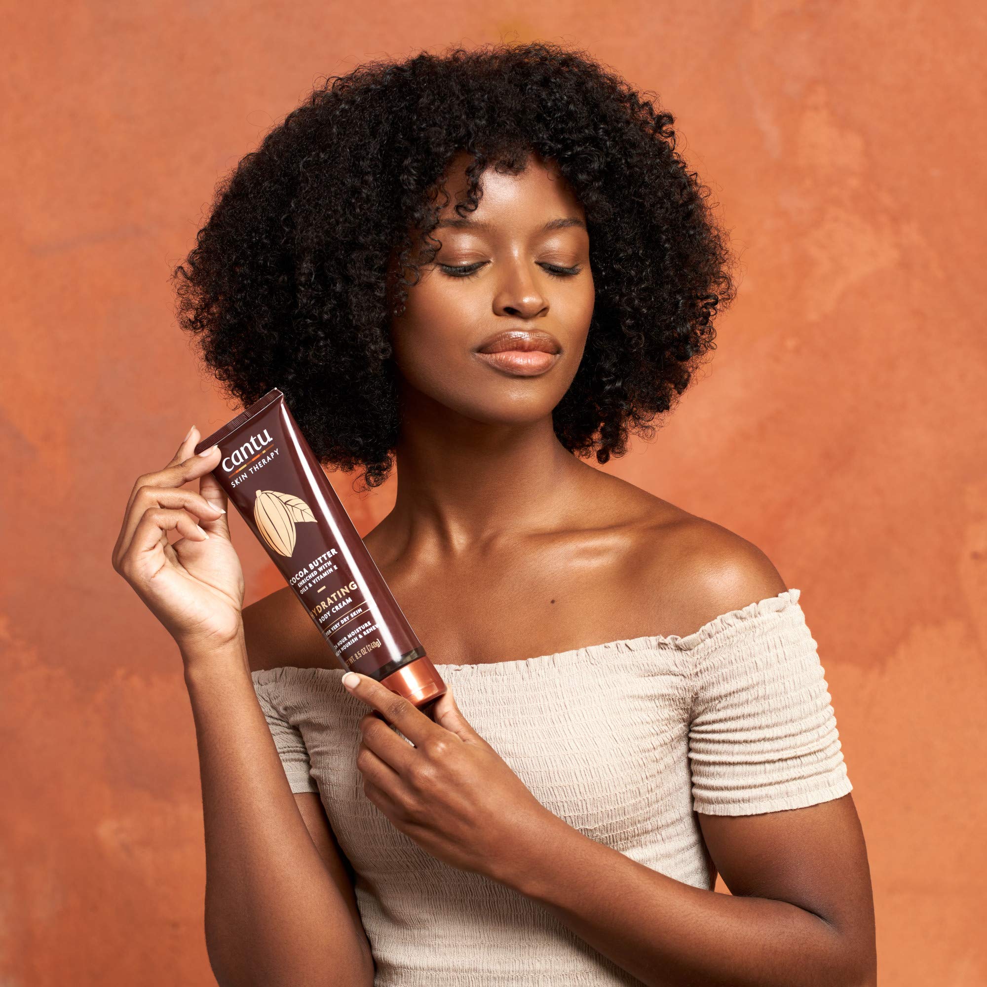 Open tub of Cantu cream with finger applying, showing easy spreadability benefit