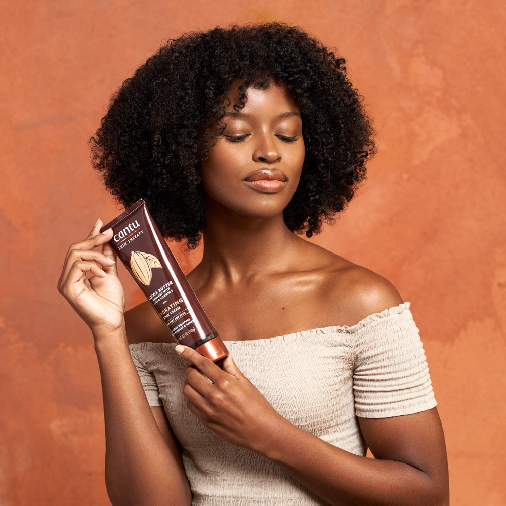 Open tub of Cantu cream with finger applying, showing easy spreadability benefit