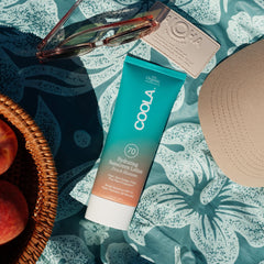 COOLA sunscreen staged on beach towel showing outdoor use and sun readiness