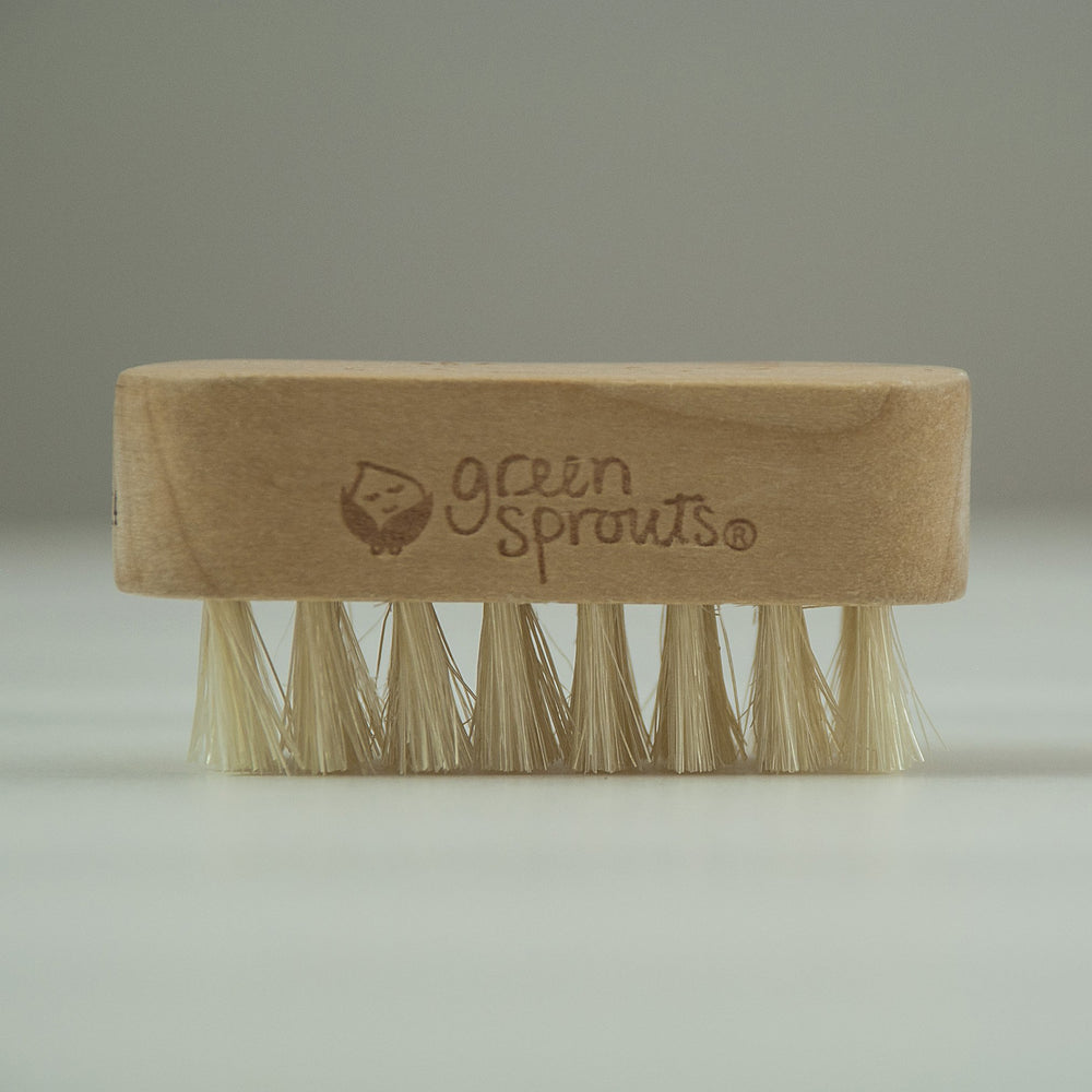 Green Sprouts brush held in adult hand over baby finger showing correct scale benefit
