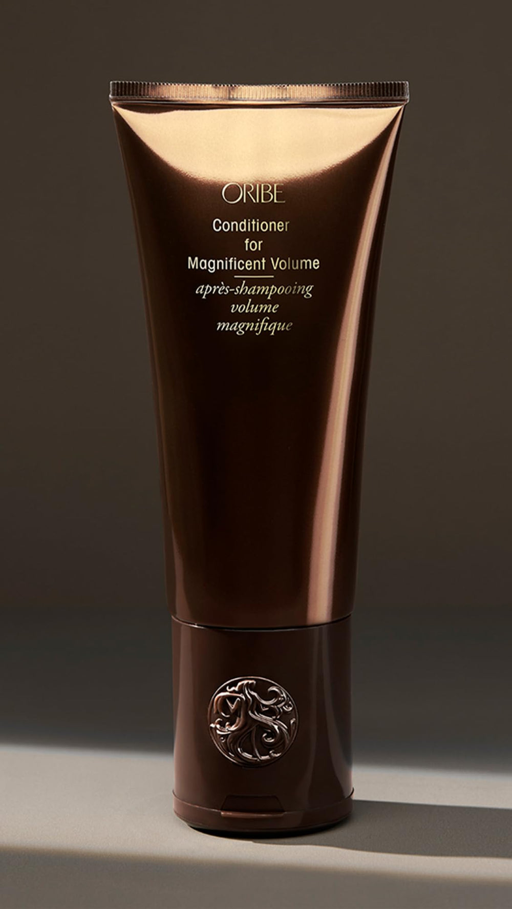 Oribe bottle next to hand showing 6.76 fl oz size and travel friendly benefit