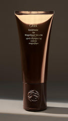 Oribe bottle next to hand showing 6.76 fl oz size and travel friendly benefit