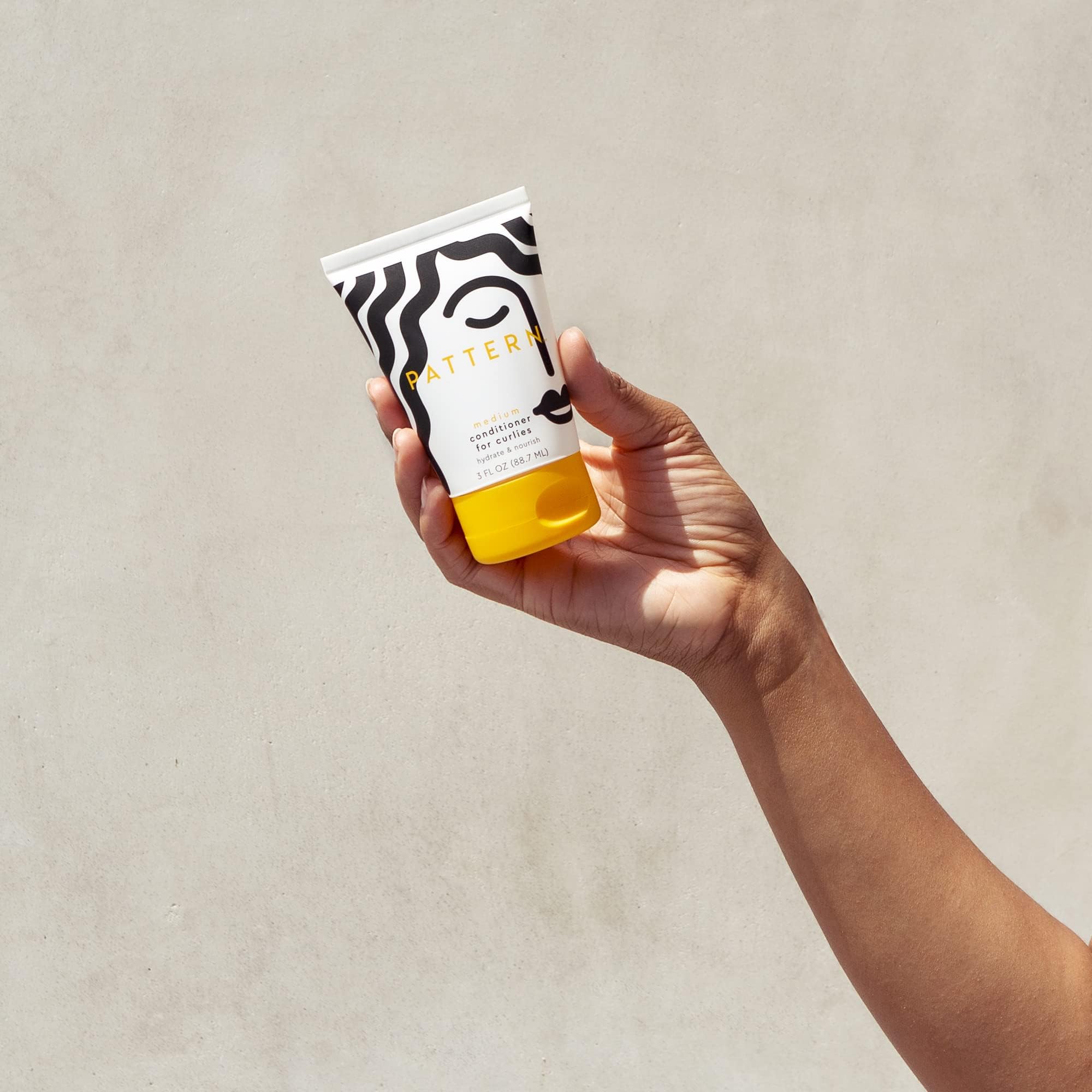 PATTERN conditioner in hand to show 3 fl oz scale for travel convenience
