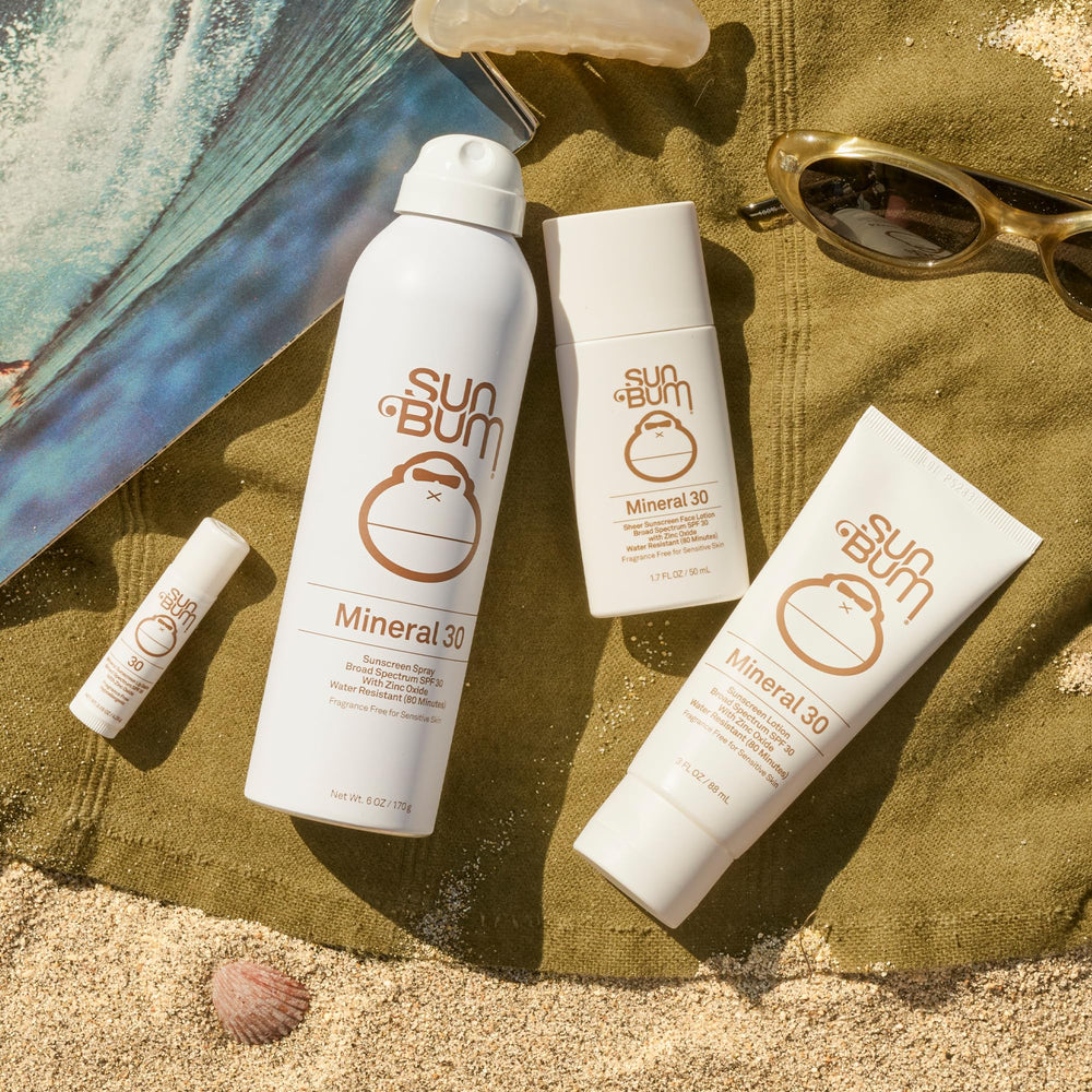 Person applying Sun Bum mineral sunscreen spray to leg at the beach demonstrating fast, full-body coverage