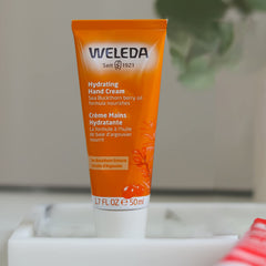Weleda sea buckthorn hand cream next to everyday items showing 1.7 fl oz travel-friendly size benefit