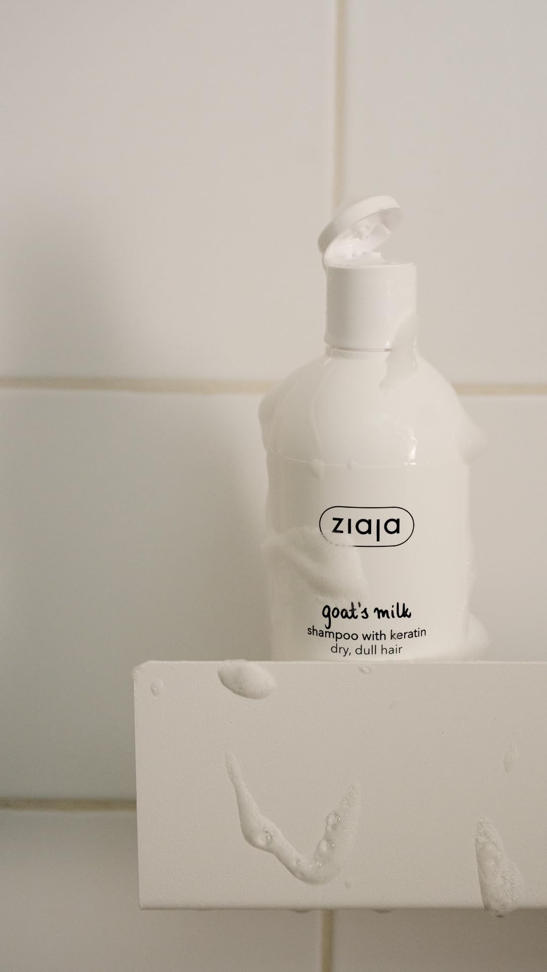 Ziaja shampoo bottle on bathroom shelf next to towel, lifestyle scene indicating easy daily use