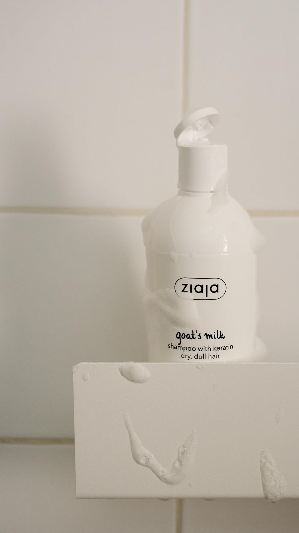 Ziaja shampoo bottle on bathroom shelf next to towel, lifestyle scene indicating easy daily use